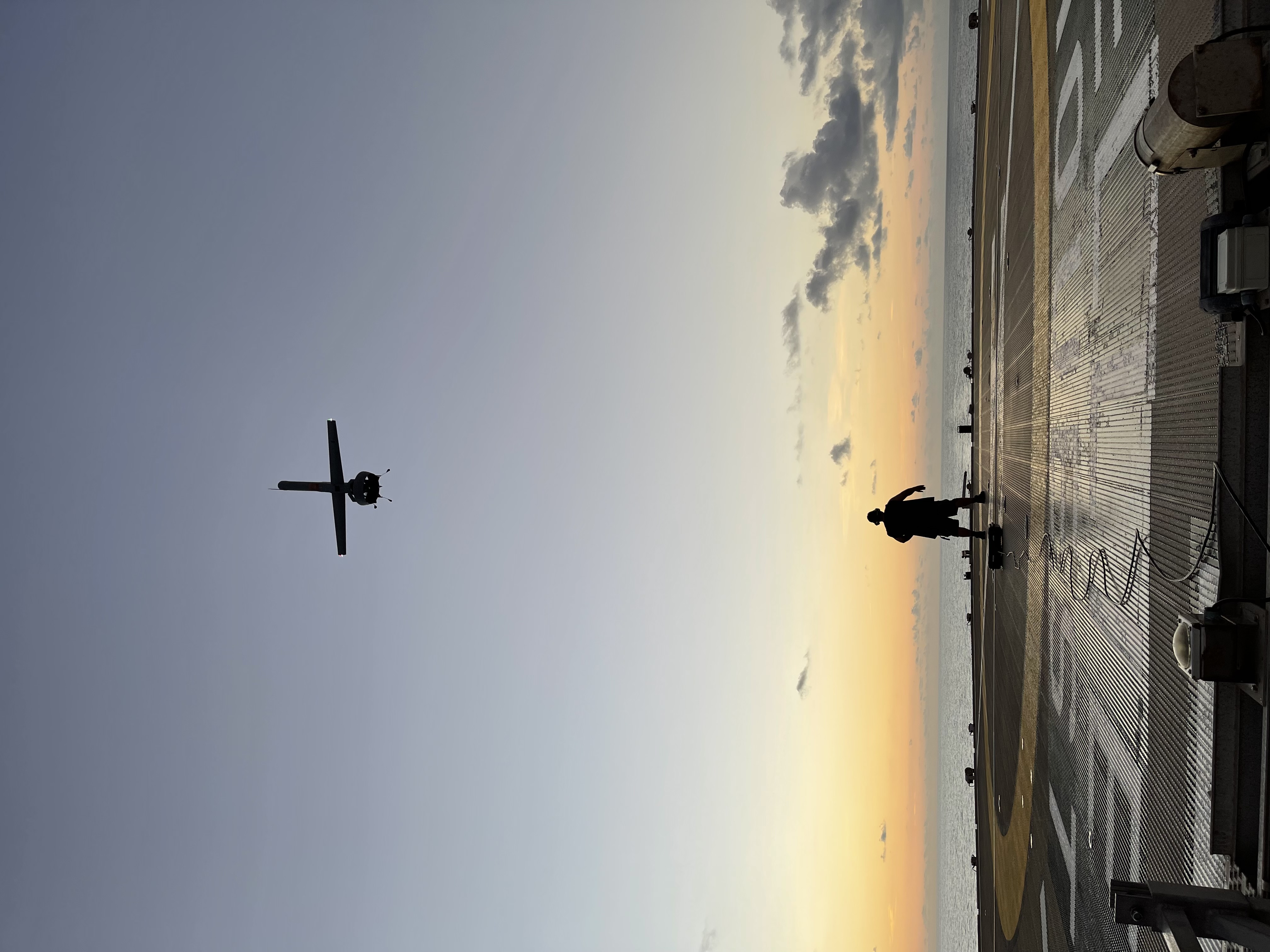 Operator on ship deck with drone overhead at sunset